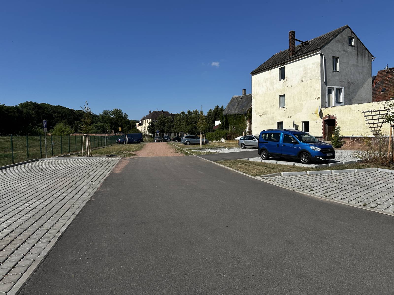Neu geordnete Zufahrt mit Asphaltfahrbahn zwischen zwei Stellplatzflächen aus Rasengittersteinen