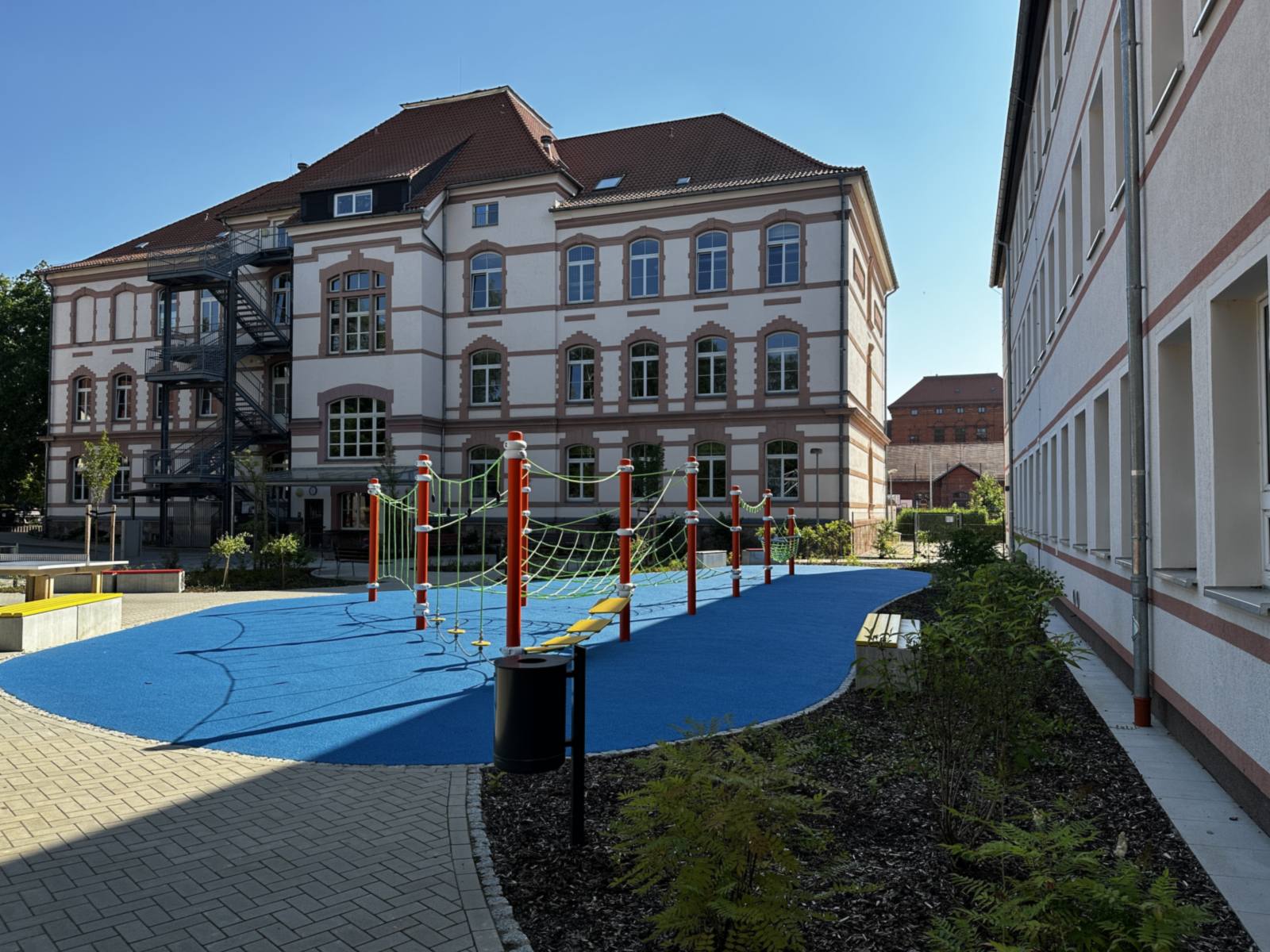 Historisches Schulgebäude mit blauem Fallschutzbelag und Kletterparcours im Schulhof