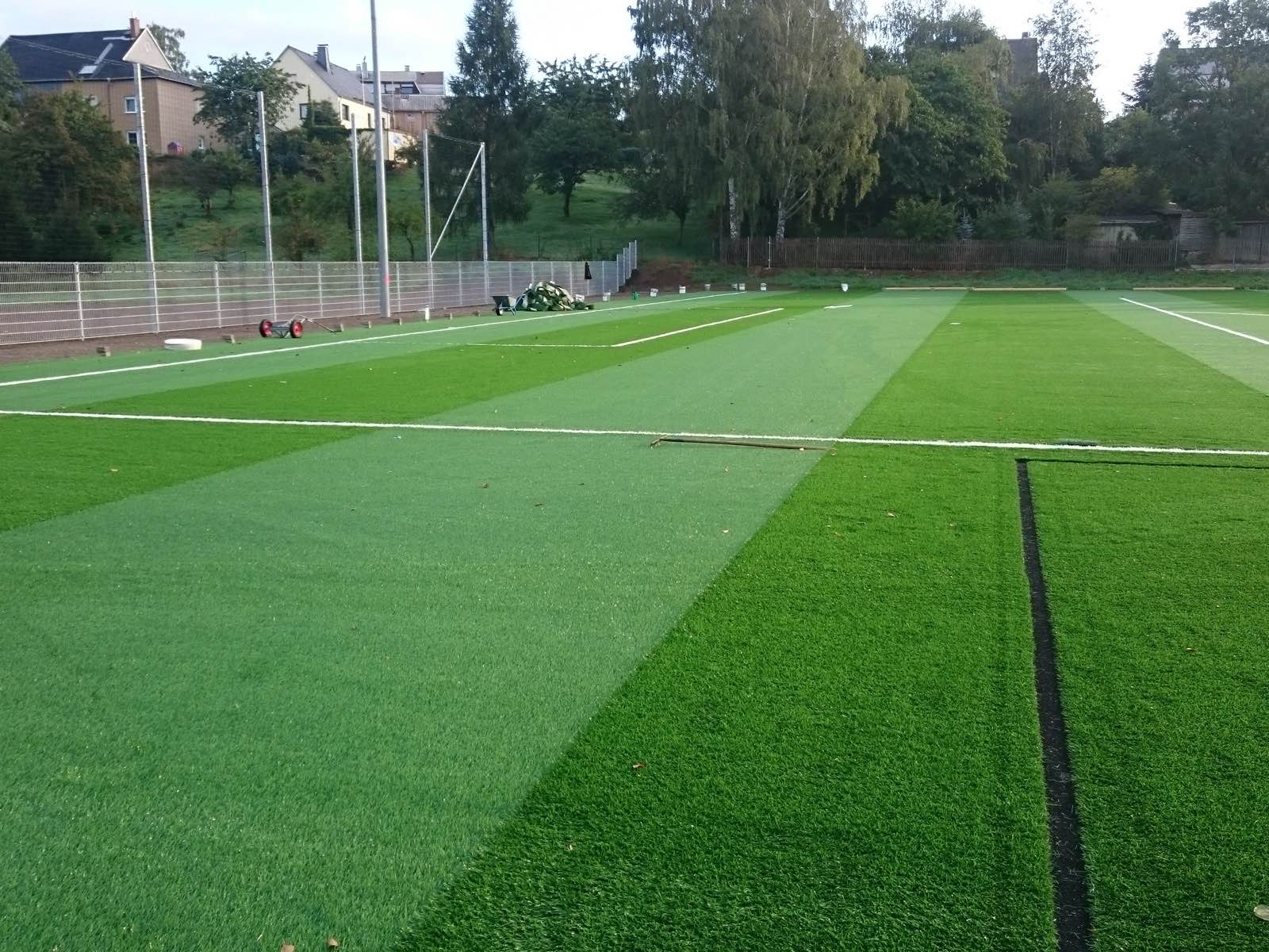 Kunstrasenbahnen mit weißen Linien und noch offenen Nähten am Spielfeld