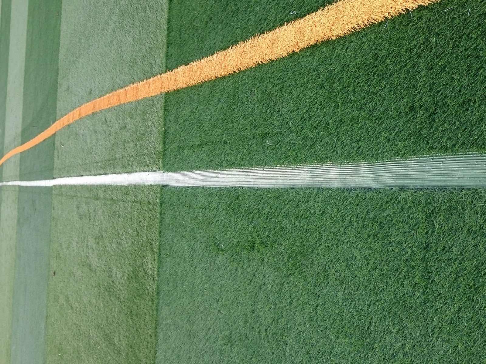 Weiße und orange Kunstrasenstreifen beim Einlegen der Spielfeldlinien