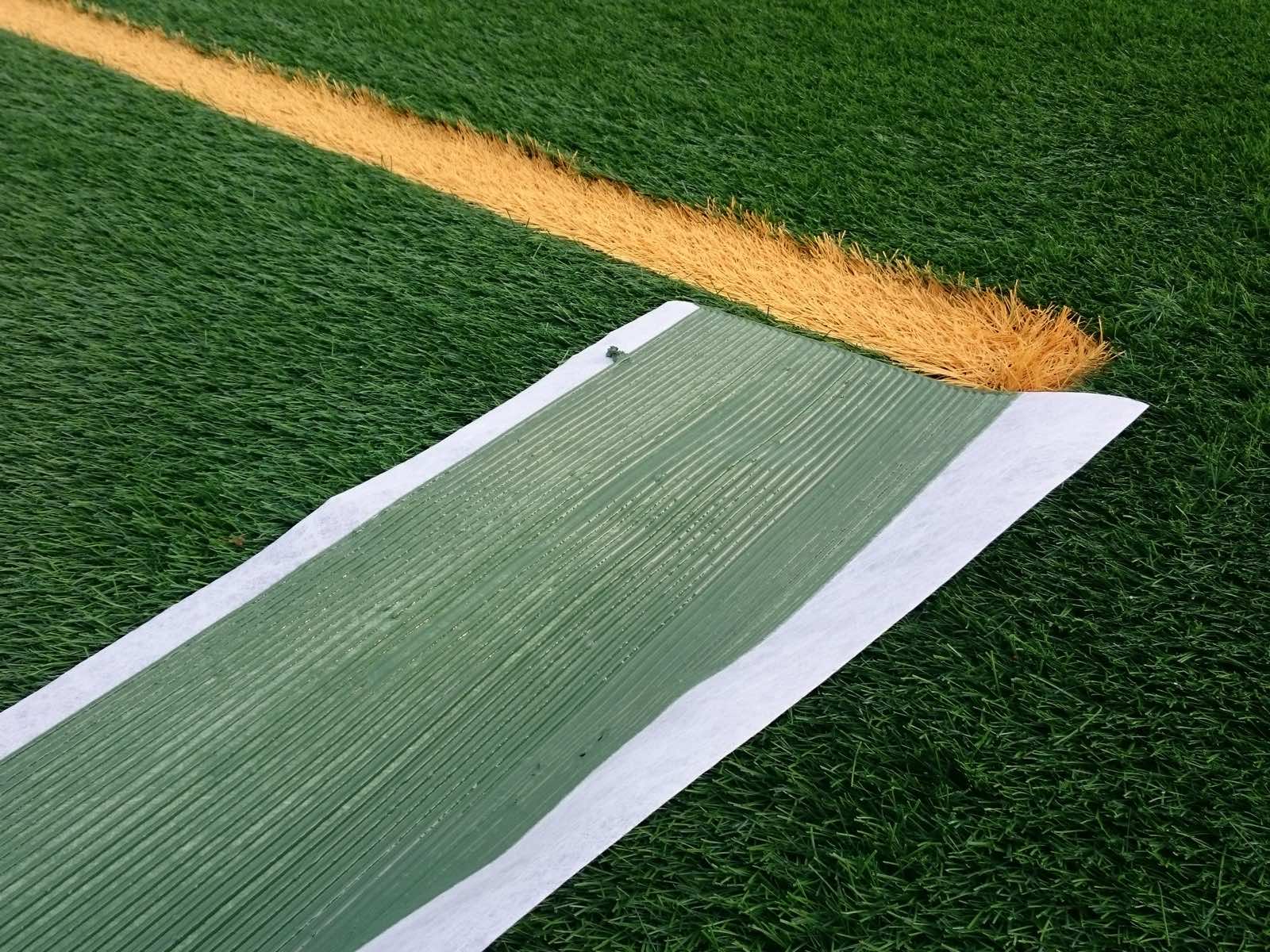 Nahaufnahme eines Nahtbands mit Klebstoff neben einer orangefarbenen Kunstrasenlinie