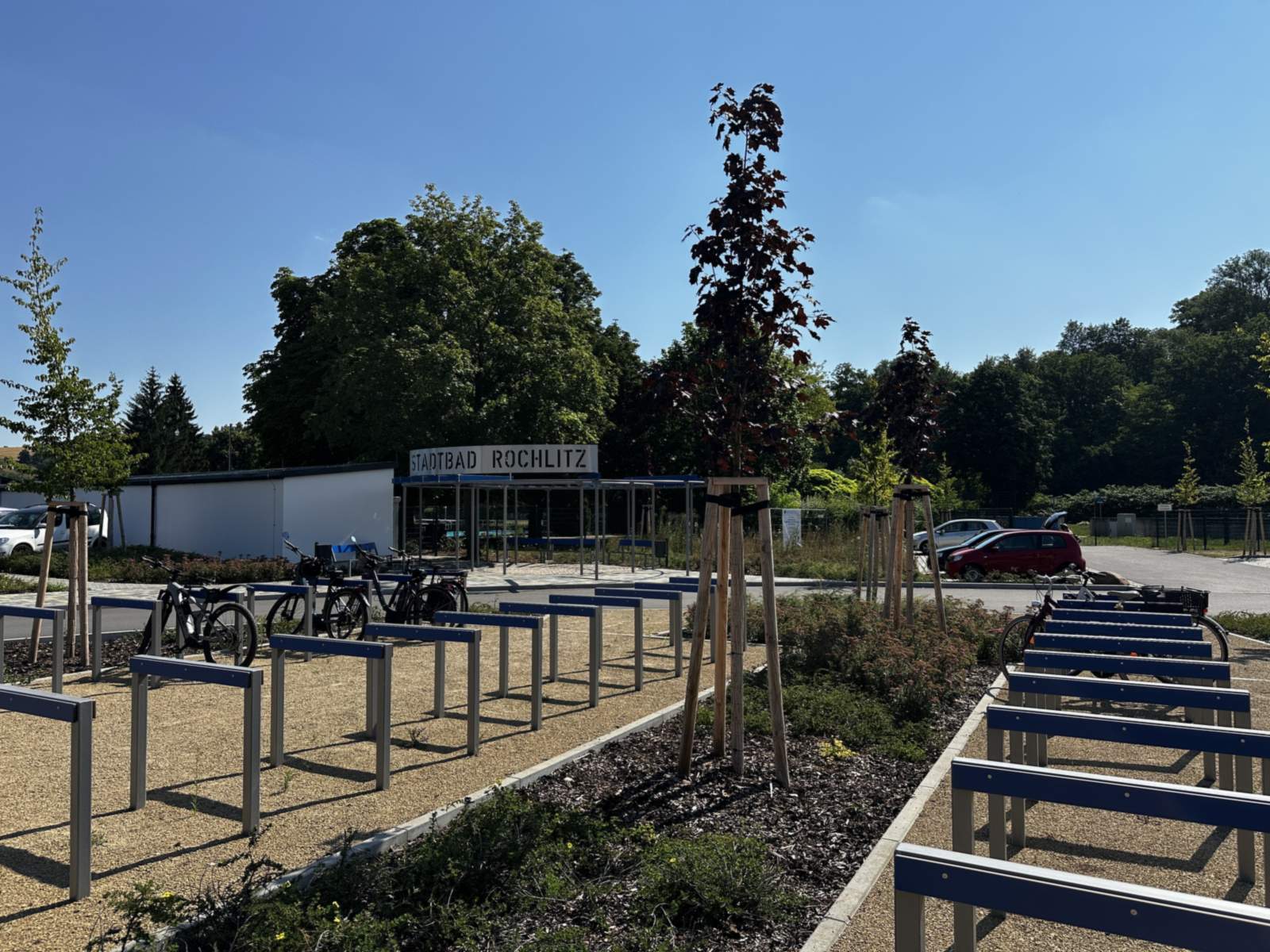 Fahrradstellplätze mit blauen Anlehnbügeln und jungen Bäumen vor dem Eingang zum Stadtbad