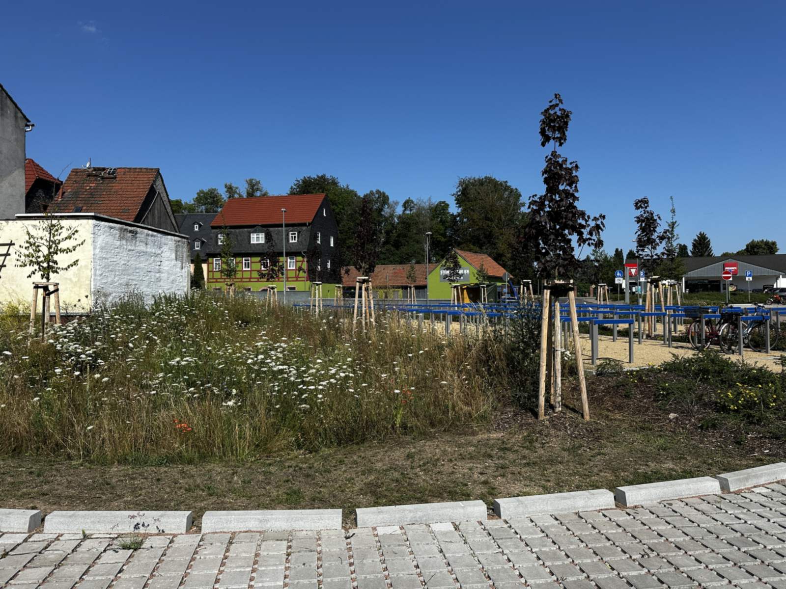 Blühende Staudenpflanzung neben dem Parkraum, im Vordergrund eine Fläche aus Rasengittersteinen