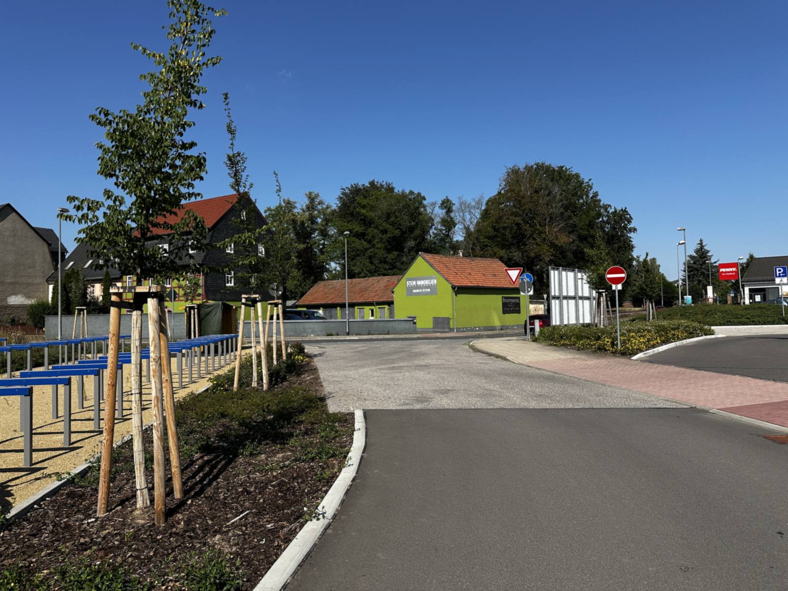 Neu geordnete Zufahrt mit Fahrbahn, Gehweg und Baumreihe am Rand des Parkraums