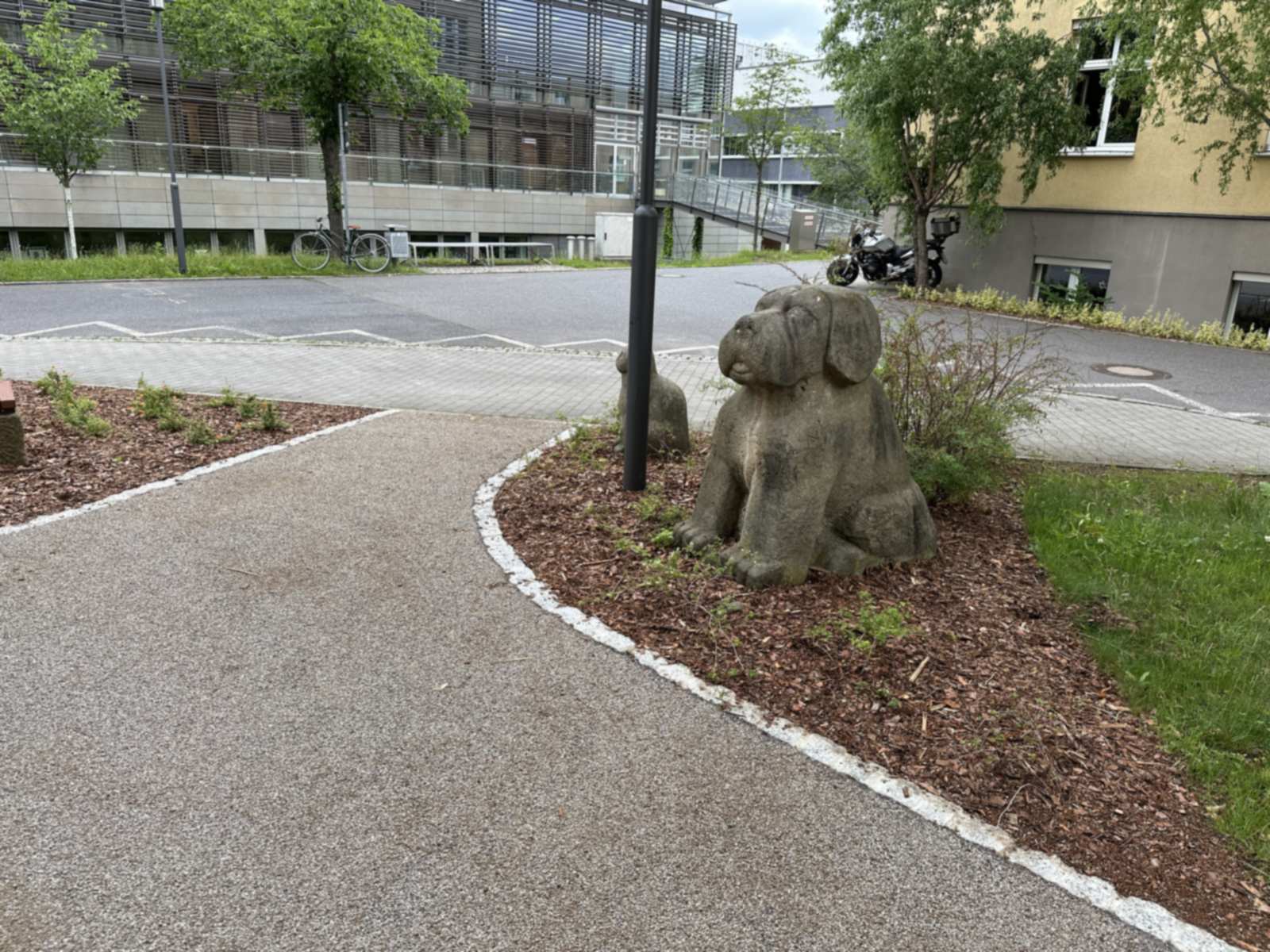 Zwei Hundeskulpturen aus Stein in einem Rindenmulchbeet am geschwungenen Weg