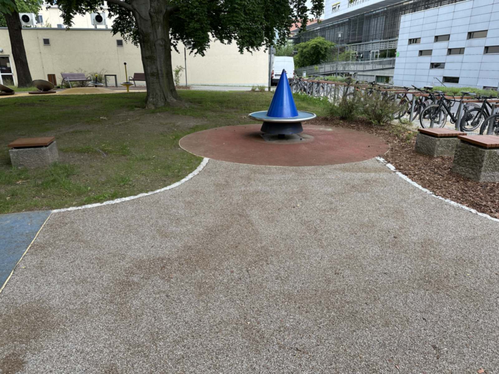 Blaues Drehspielgerät auf rundem rotem Belag, dahinter Fahrradstellplätze