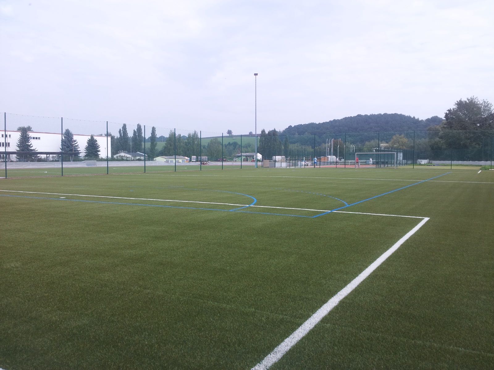 Kunstrasenplatz mit weißen und blauen Spielfeldlinien und Ballfangzaun